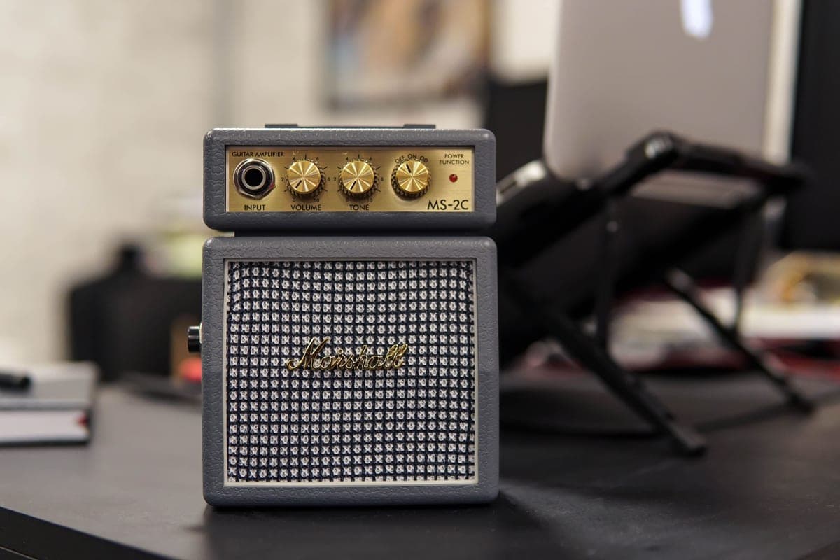 A small practice amplifier on a desk beside a guitar