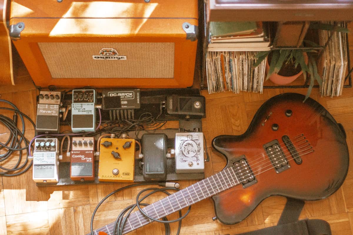 An orange distortion pedal on a dark wooden floor
